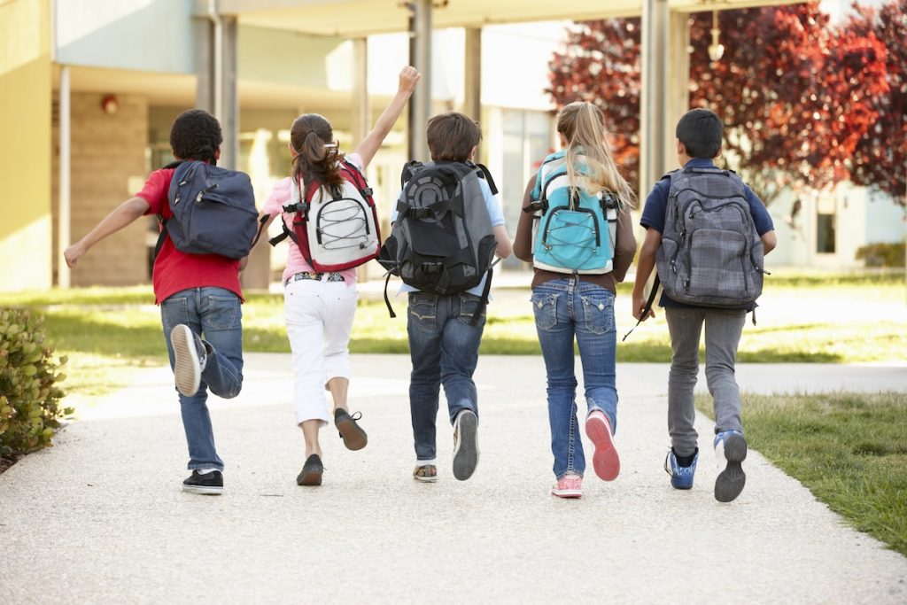 Education Freedom Tax Credit: Who Qualifies and When Diverse group of smiling elementary school children running away from the camera down a sunny walkway lined with trees and school buildings. The children are wearing backpacks, representing the broad range of K-12 students who could benefit from the new Education Freedom Tax Credit, which aims to fund scholarships for public, private, and charter school expenses. Source: The College Investor