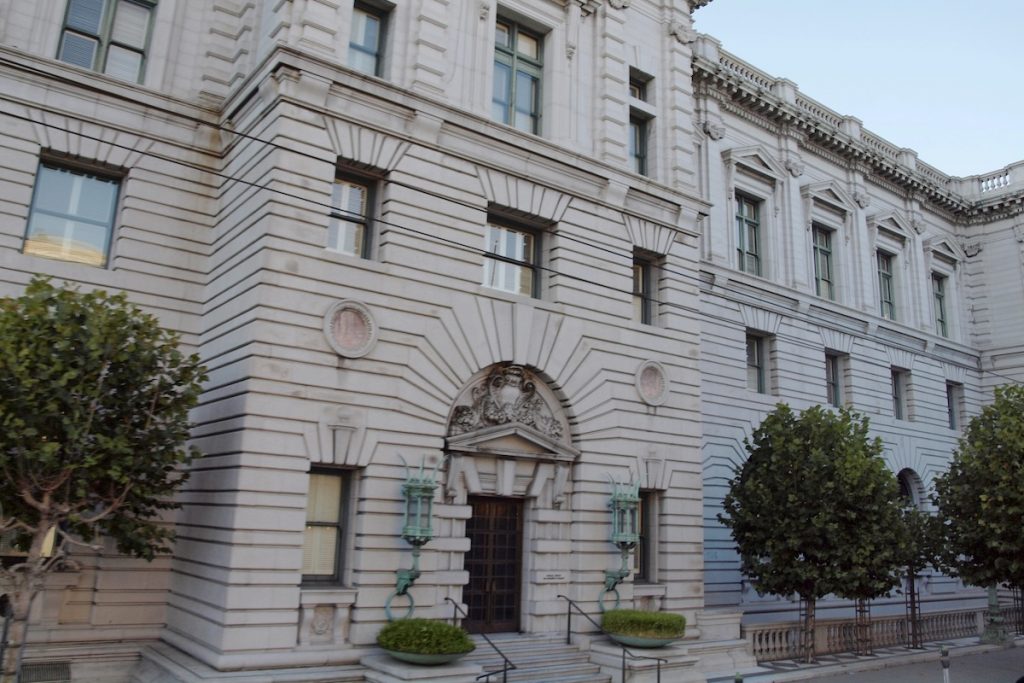 Exterior view of a grand, historic federal courthouse featuring classical stone architecture, rusticated walls, and an ornate arched entrance flanked by decorative green lantern fixtures. This stately building represents the Ninth Circuit Court of Appeals, the judicial battleground where the Education Department is currently arguing its motion to delay the Sweet v. McMahon borrower defense settlement—a critical legal decision that could impact up to $12 billion in debt relief for defrauded student loan borrowers. Source: The College Investor