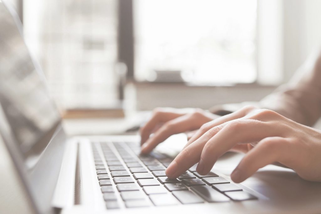 Close-up of a student’s hands typing on a silver laptop keyboard next to textbooks and glasses. This image visualizes the urgency and focus required when applying for mid-year student loans or an Education Line of Credit to cover unexpected college expenses like housing or course fees after the semester has already begun. Source: The College Investor