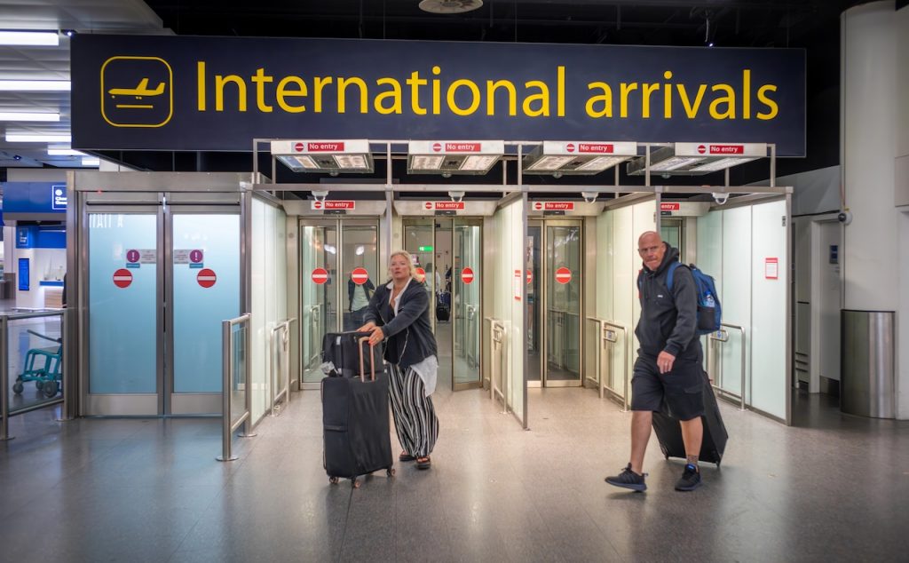 Male and female passengers with luggage walk through International Arrivals at airport, reflecting the change in international student enrollment at US colleges.