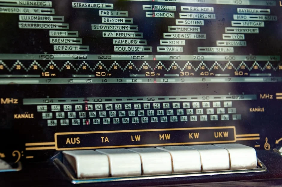 When the U.S. military finally deployed frequency-hopping spread spectrum on Navy ships during the 1962 Cuban Missile Crisis blockade, the patent that described the technique had expired three years earlier, and its inventor was watching the news in a Los Angeles bungalow without any idea her idea was at sea. Close-up of a vintage radio dial displaying frequency bands and station names.